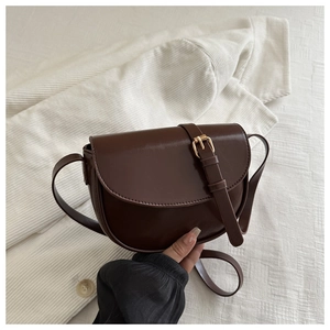 Detail of dark brown semi-circular saddle bag with gold metal buckle and smooth PU finish