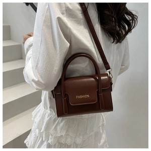 Detail of dark brown leather handbag featuring golden hardware and FASHION lettering