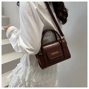 Detail view of deep brown faux leather handbag with gold Fashion text on the white dress