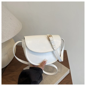 White saddle bag made of glossy PU leather with adjustable shoulder strap on wooden table