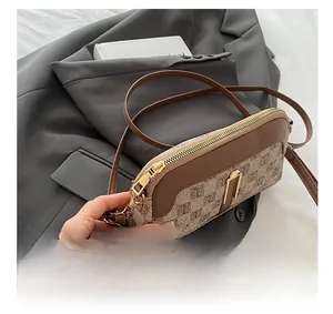 Gros plan sur la fermeture éclair dorée et le motif monogramme du sac à bandoulière
