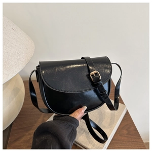 Detail of a sleek black saddle bag with glossy finish and gold buckle adjustment