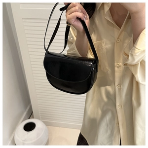 Close-up of glossy black leather saddle bag with gold metal buckle and adjustable strap