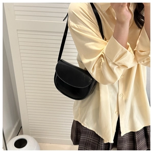 Black half-moon saddle bag worn as an underarm shoulder bag with a matte leather texture
