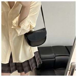 Detail view of a black glossy leather saddle bag worn by a model in a minimalist setting
