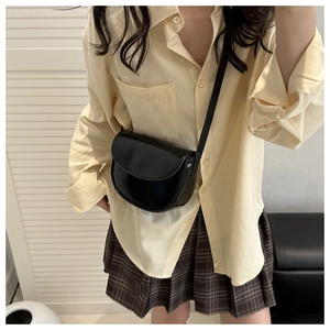 Detail shot of glossy black saddle bag crossbody on a yellow shirt and plaid skirt