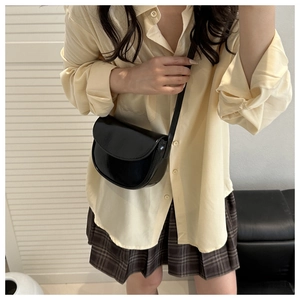 Glossy black crescent crossbody bag styled with a schoolgirl pleated skirt outfit