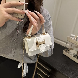 White mini handbag with gold H buckle and chain strap held by a model in a cozy room