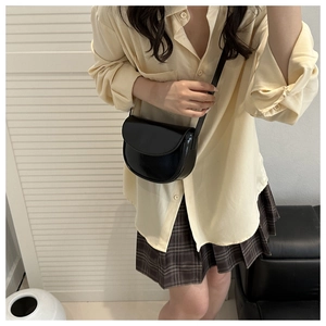 Model wearing a black matte PU leather saddle crossbody bag with a minimalist flap design