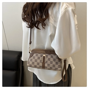 Détail d'un sac coquille beige à monogramme avec bordure en cuir marron et zip doré
