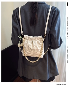 Detail of cream quilted backpack with gold chain strap and tulip charm on grey blazer