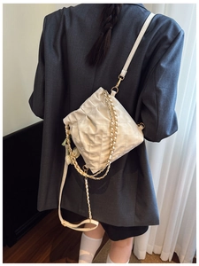 Detail of white quilted bucket bag shown as a backpack on model with chain strap