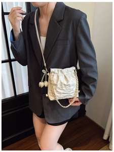 Elegant beige quilted bucket bag with chain strap and tulip charm worn by a model