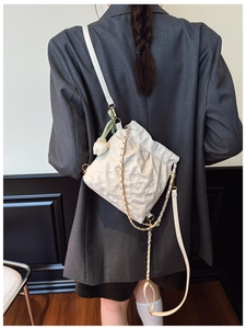 Quilted cream crossbody bag with gold chain strap and floral charm on a female model