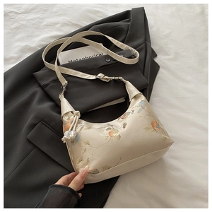 Detail of bird and floral embroidery on a beige crossbody bag with pearl charms