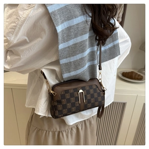 Détail d'un sac à bandoulière marron à carreaux avec motif en T porté par un mannequin