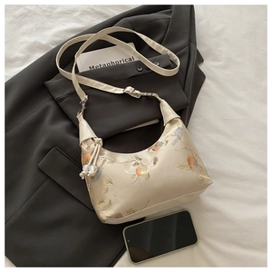 Detail of cream crescent bag featuring intricate floral embroidery and pearl tassel