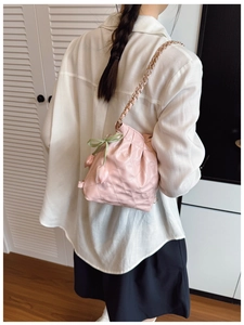 Close-up of pink quilted bucket bag with gold chain, green bow, and tulip charms