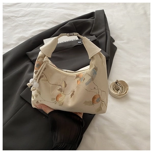 Detail of floral and bird embroidery on a beige crossbody bag with unique knotted handles