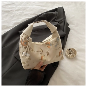 Detail of oriental embroidery on off-white crossbody bag with unique knot handle