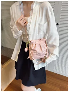 Detail of pink quilted bucket bag with gold chain strap and tulip charm on model