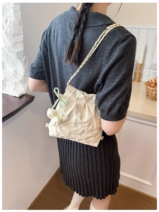 Quilted white bucket bag with chain strap and floral charm shown on model's back
