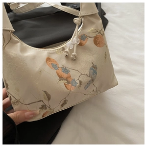 Close-up of cream shoulder bag featuring elegant bird and persimmon embroidery details