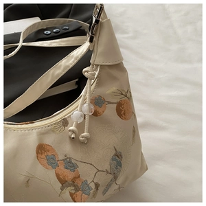 Detail of floral jacquard embroidery with bird and persimmon patterns on beige shoulder bag