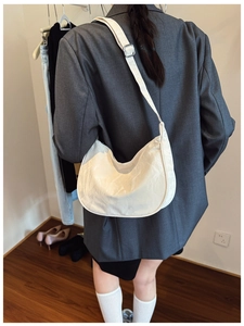 Detail of a creamy off-white crescent crossbody bag with textured pleats and wide strap