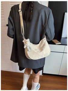 Detail of a beige hobo bag with teddy bear pendant worn on a model's shoulder