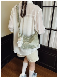 Detail of light green crescent bag with pleated texture and white plush bear pendant