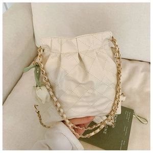 Detail of cream quilted bucket bag with gold chain strap and a white tulip charm