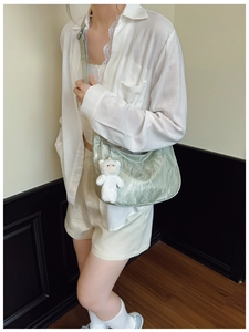 Detailed view of light green pleated handbag with cute white plush bear charm accessory