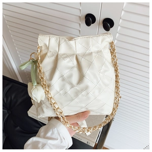Close-up of quilted cream bucket bag with gold chain and floral bow charms