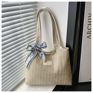 Detail of woven straw tote bag featuring decorative blue silk scarf and leather nameplate