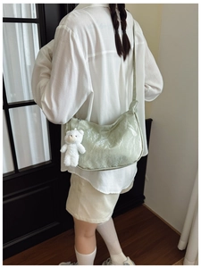 Close-up of light green glossy hobo bag with pleated texture and white plush bear charm