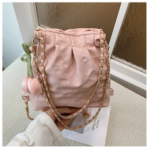 Detail of light pink quilted chain bag featuring tulip charm and woven metal strap