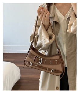 Detail of a brown canvas and leather underarm bag with punk buckles on a model