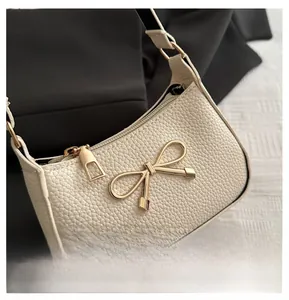Detail of cream pebbled leather handbag featuring a decorative gold bow buckle closure