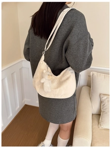 Chic beige crescent shoulder bag with plush bear charm shown on model in a cozy setting