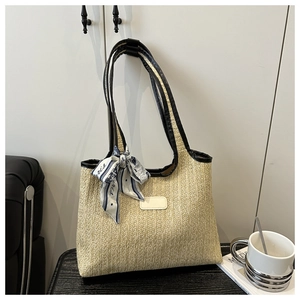 Close-up of woven straw tote bag with black leather handles and printed silk scarf detail