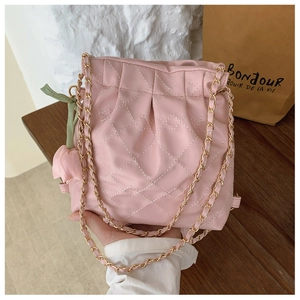 Detail of pink quilted crossbody bag with gold chain strap and floral charm accessory