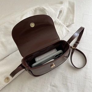 Dark brown matte leather saddle bag showing spacious interior with smartphone and earbuds
