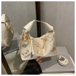 Detailed embroidery of birds and flowers on a cream silk handbag with metallic buckle