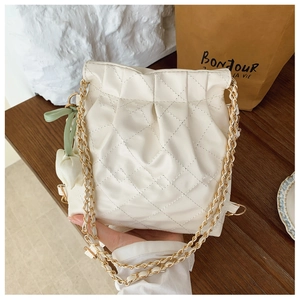 Detail of white quilted bucket bag featuring gold chain and floral ribbon charm