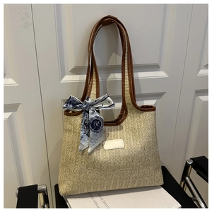 Detail of woven straw tote bag with brown leather handles and decorative silk scarf