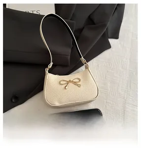 Close-up of litchi-textured beige shoulder bag with golden bow hardware detail