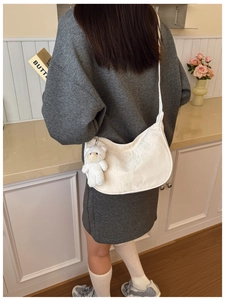 Detailed texture of white crescent bag featuring a plush bear charm and wide strap