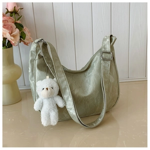Detail of light green pleated crescent bag with a cute white teddy bear charm