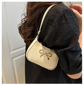 Détail d'un sac sous le bras blanc cassé avec fermoir nœud doré porté par un modèle